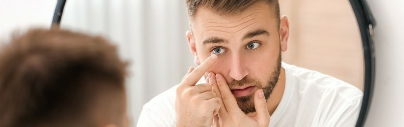 Uomo che applica o rimuove una lente a contatto allo specchio - consigli per la gestione corretta in estate